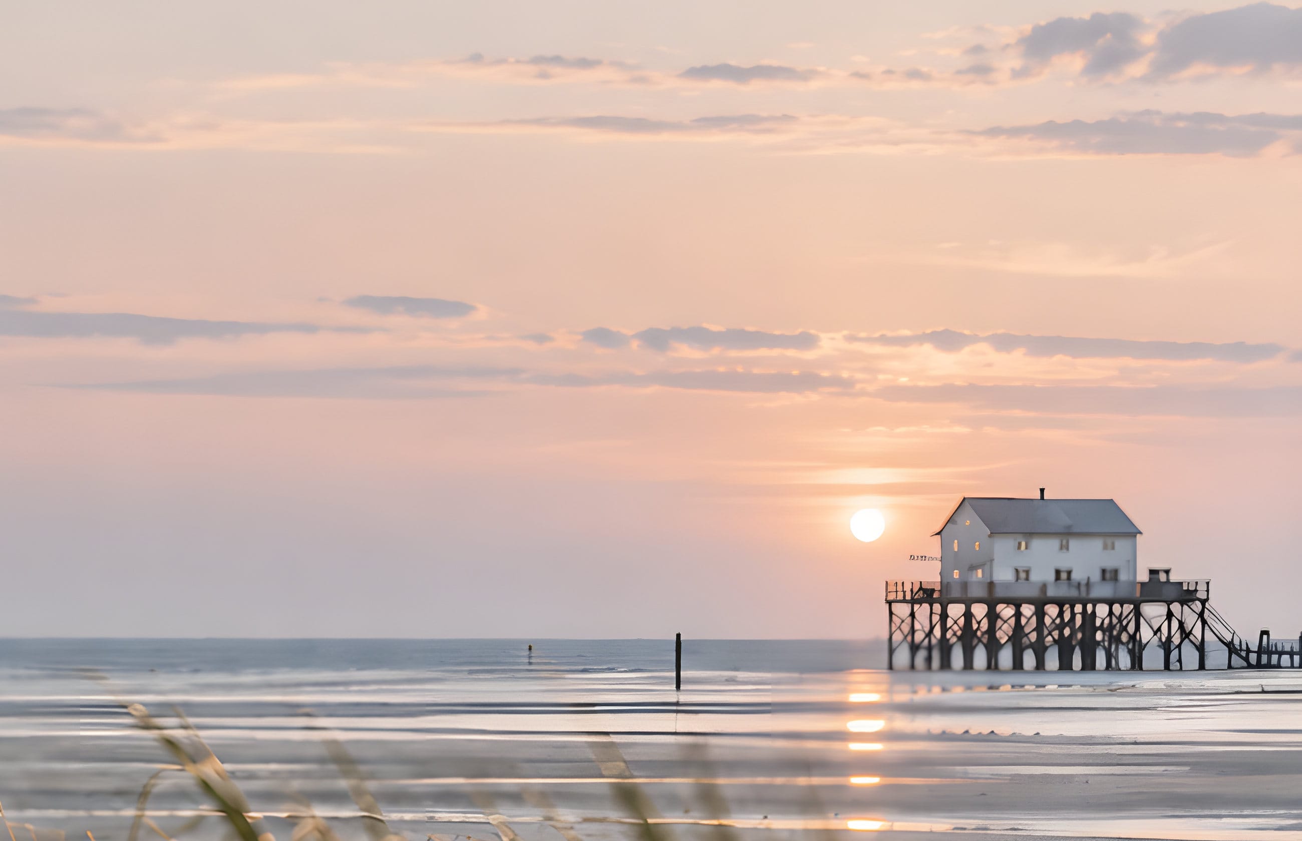 Sonnenuntergang am Strand von Sankt Peter-Ording mit Pfahlbau und Dünengras
